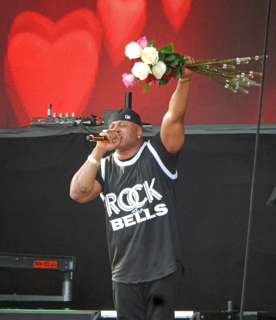 LL Cool J performing live in a Rock The Bells jersey, holding roses and a microphone on stage
