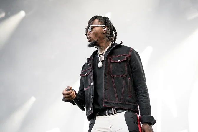 Offset on stage in a black-and-red denim jacket and chain, showing his signature fashion style