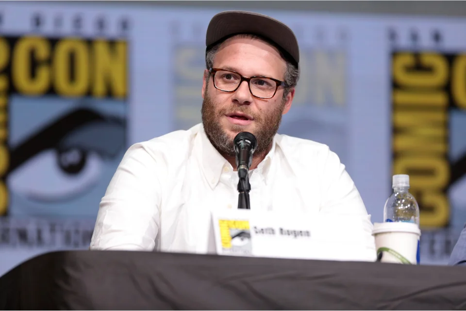 Seth Rogen speaking at a Comic-Con panel with a name card in front of him
