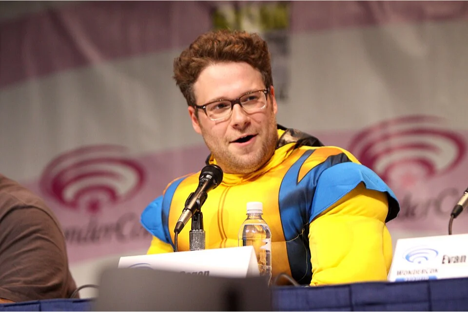 Seth Rogen speaking at a WonderCon panel wearing a yellow superhero costume