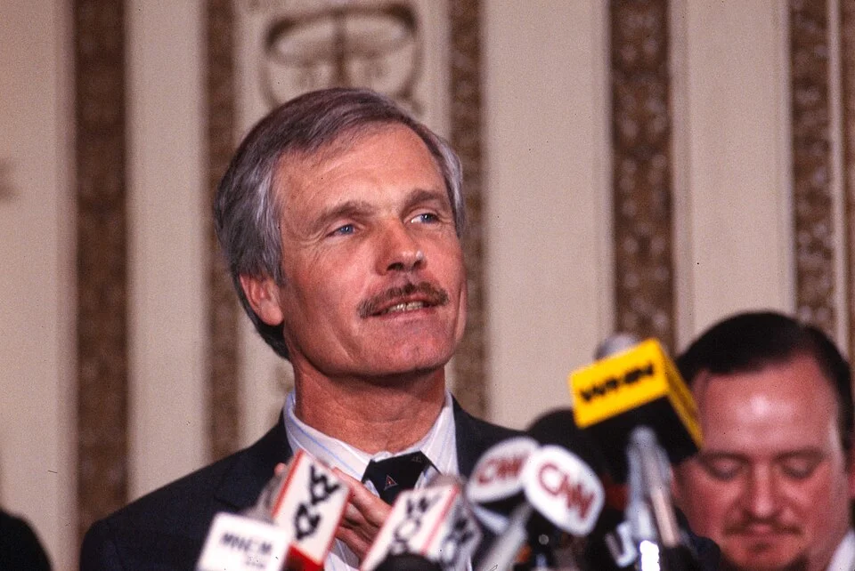 Ted Turner at a 1985 press conference surrounded by microphones including CNN
