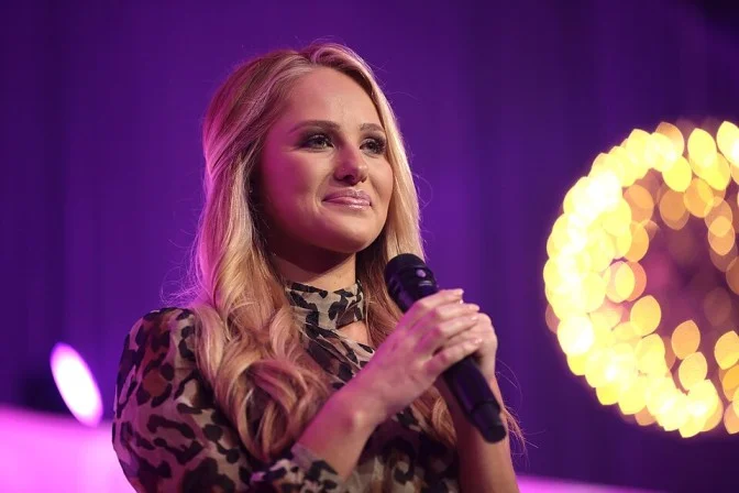 Tomi Lahren speaking at an event, holding a microphone