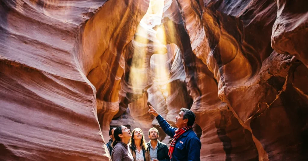 Navajo tour guide pointing at dramatic light beams inside Antelope Canyon slot canyon to visiting group