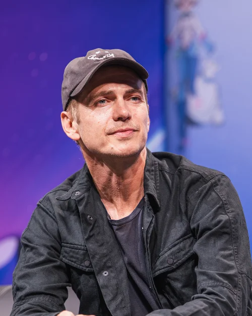 Hayden Christensen in a cap and black jacket on a fan convention panel stage during his 2026 Star Wars return