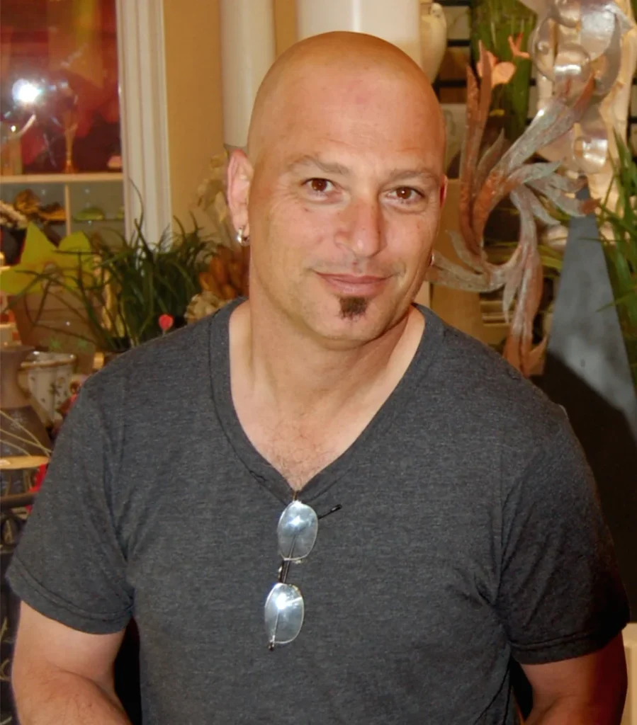 Howie Mandel in a grey t-shirt with sunglasses hanging at his collar during his America's Got Talent years
