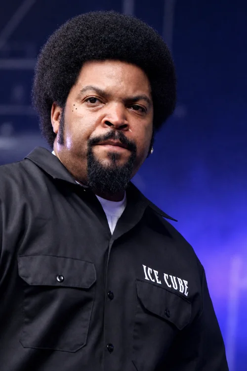 Ice Cube portrait 2026 - Rapper and BIG3 founder wearing black shirt with his name embroidered, photographed against blue background during business promotion