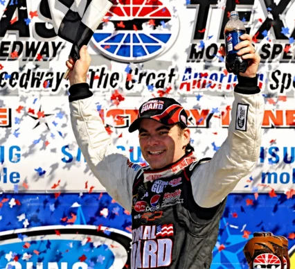"Jeff Gordon NASCAR victory lane celebration - Four-time Cup Series champion driver with trophy and confetti at racetrack podium"