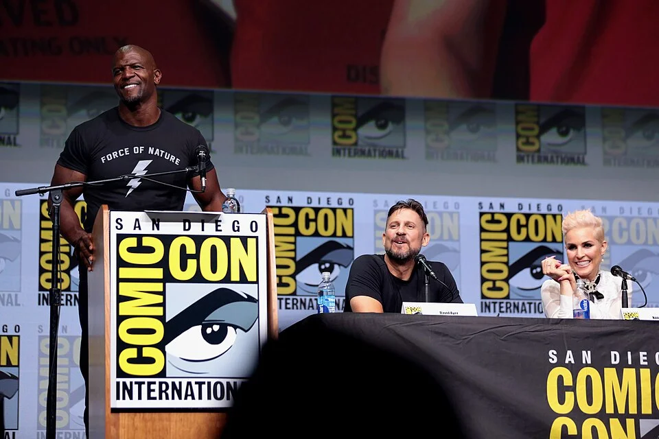 "Terry Crews speaking at San Diego Comic-Con panel, wearing black Force of Nature t-shirt at podium with Comic-Con International branding visible"