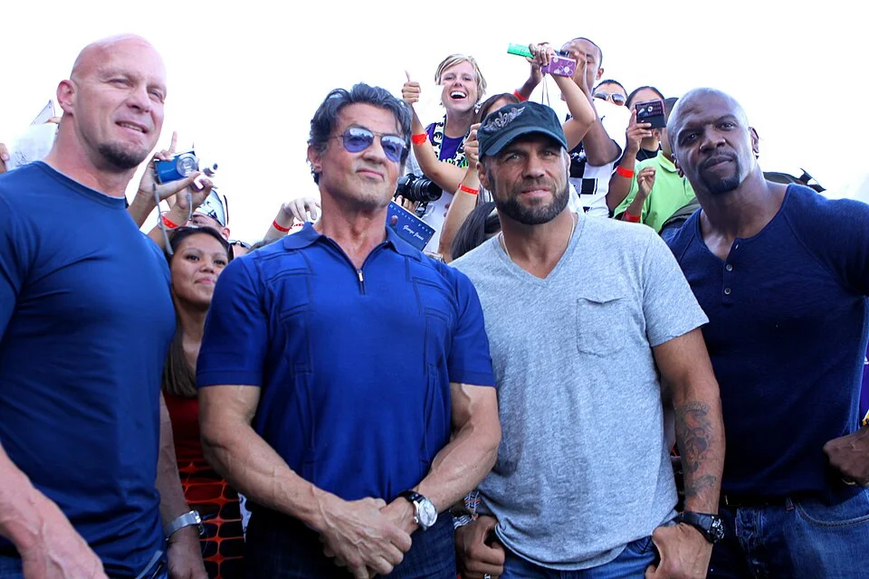 Terry Crews (far right) standing with Steve Austin, Sylvester Stallone, and Randy Couture at an outdoor fan event