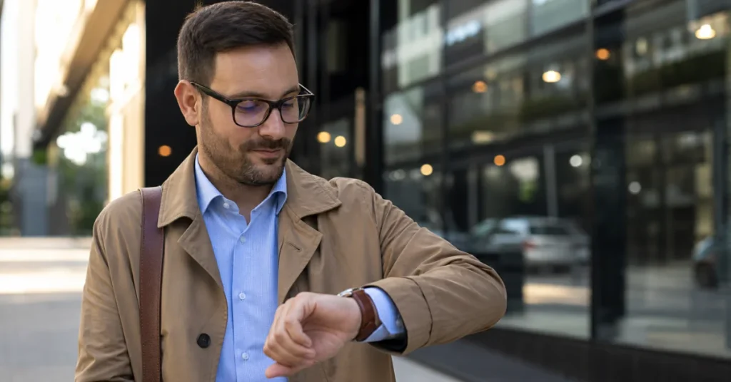 Are Tissot watches good: a man in a tan coat checking his wristwatch on a city street, everyday wear