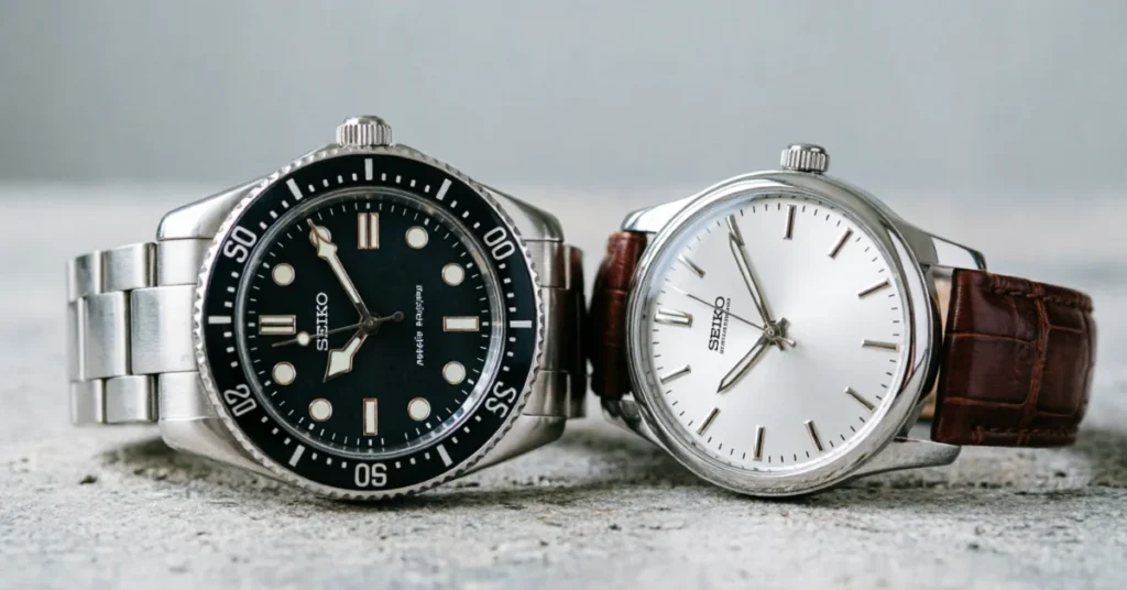 Seiko diver with black bezel next to a Seiko dress watch on a leather strap, side by side on stone