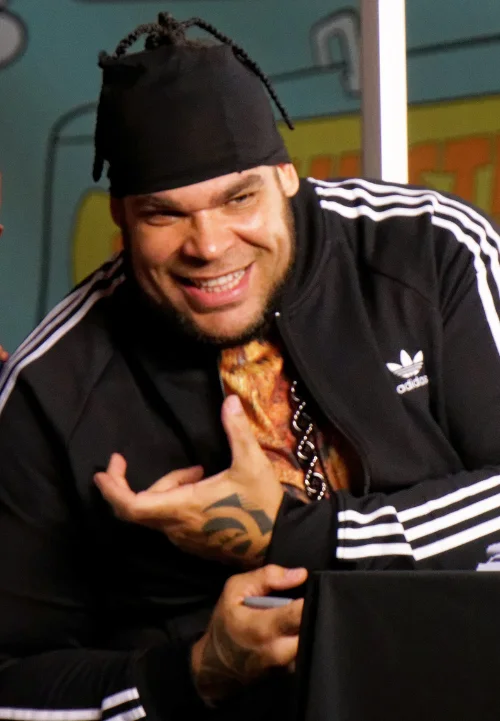 Tyrus smiling and gesturing in a black Adidas jacket at a public appearance
