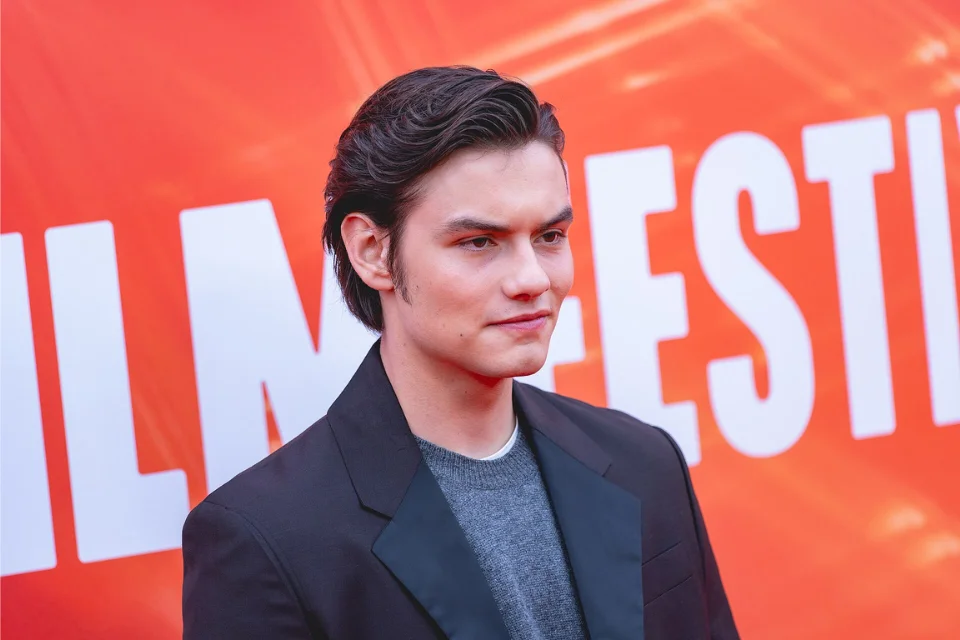Louis Partridge in a black blazer against an orange film festival backdrop