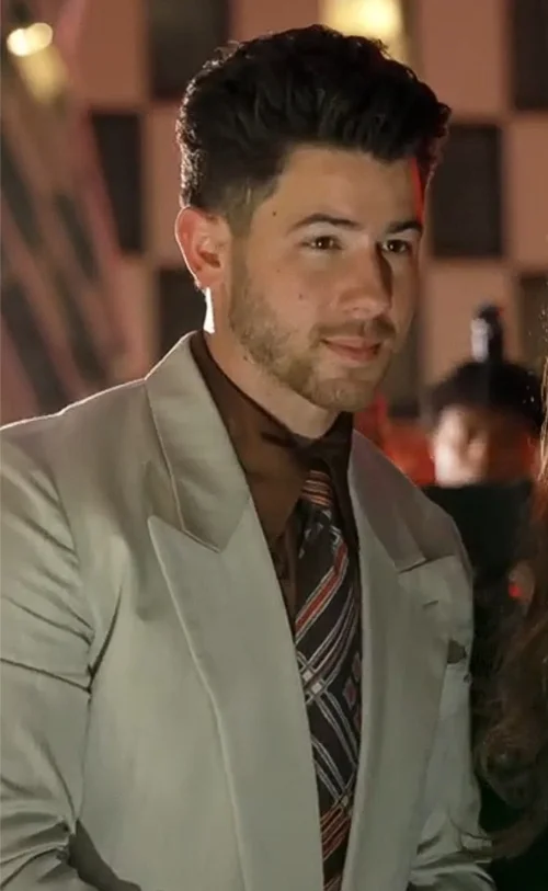 Nick Jonas in a light gray suit and striped tie at an evening event