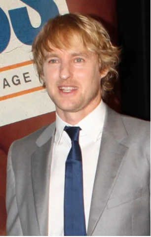 Owen Wilson smiling in a gray suit and navy tie