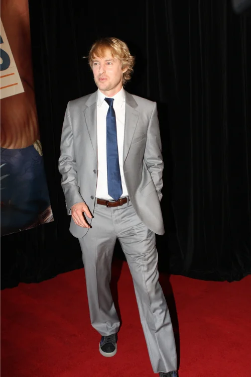 Owen Wilson full-body on a red carpet in a gray suit