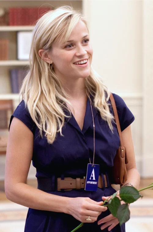 "Reese Witherspoon in navy dress holding rose, actress and producer with $400-450 million net worth"