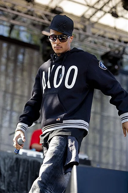 T.I. on stage wearing his own AKOO brand hoodie, black cap, and sunglasses, holding a microphone