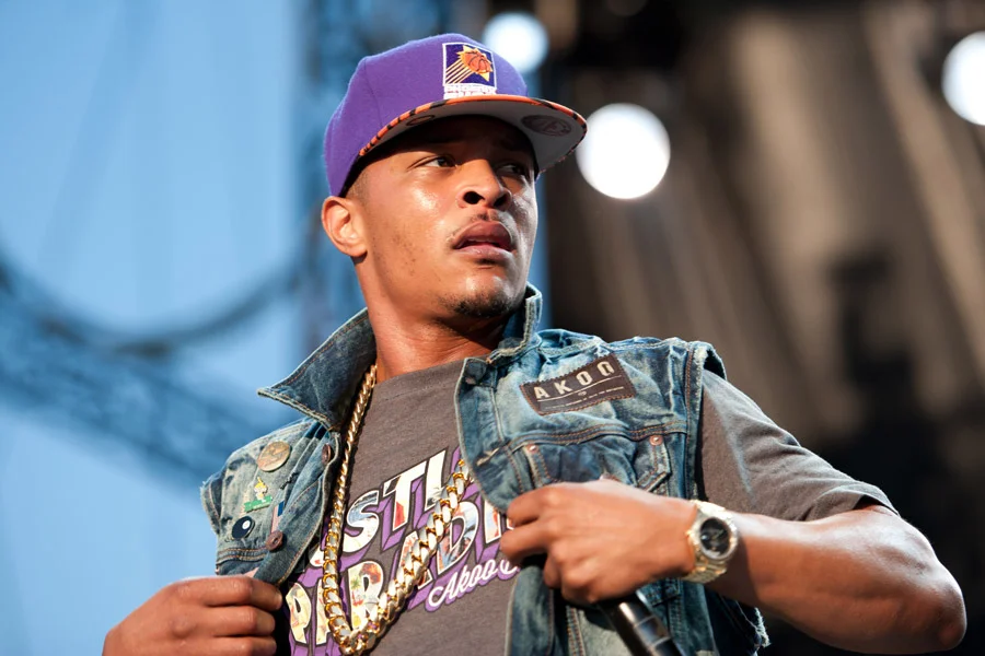 Clifford "T.I." Harris performing on stage wearing a purple Phoenix Suns cap, AKOO denim vest, and gold chain