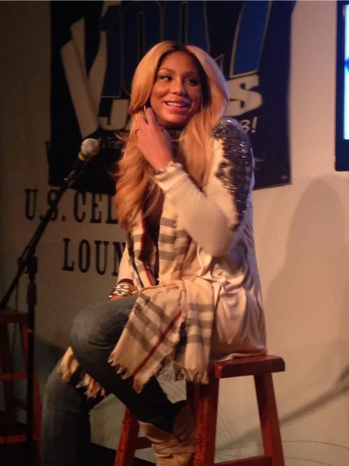 Tamar Braxton smiling on a stool beside a microphone at a U.S. Cellular Lounge appearance