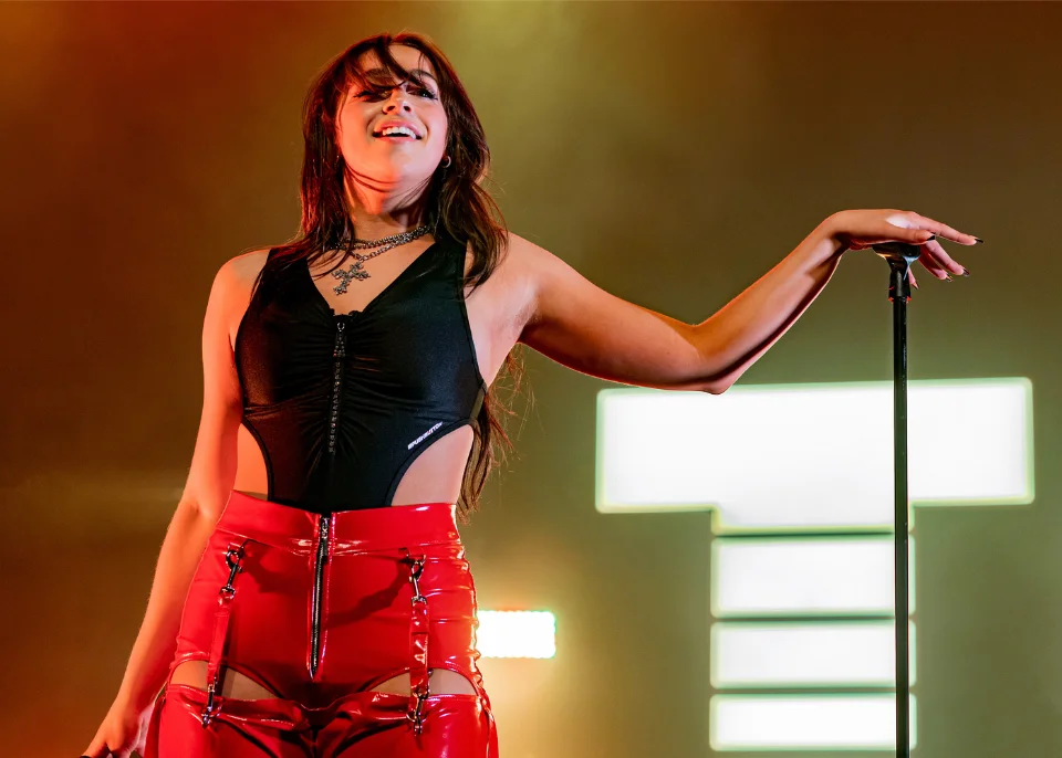 Tate McRae smiling mid-performance on the Miss Possessive World Tour in a black cutout bodysuit and red vinyl pants