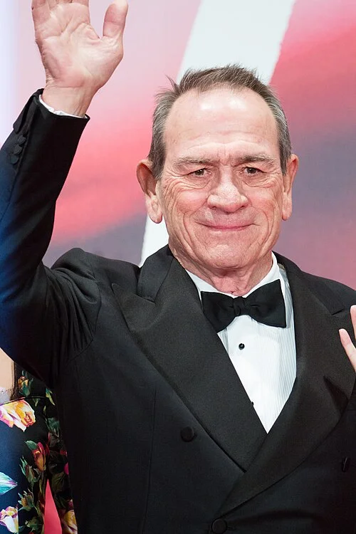 Tommy Lee Jones in a tuxedo and bow tie waving on the red carpet