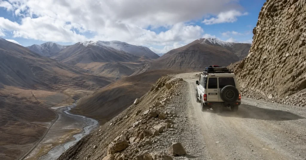 Best places to travel in Central Asia: a 4x4 with roof luggage driving a gravel ledge road through the Pamir mountains in Tajikistan
