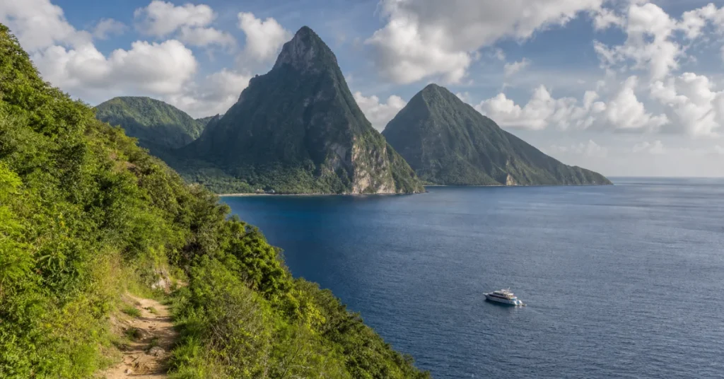 Caribbean islands to visit: Saint Lucia's twin Pitons rising from the sea with a hiking trail in the foreground and a boat for scale