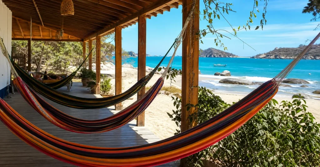 Cheapest countries to visit in South America: colorful hammocks on a beachfront hostel porch with a traveler relaxing above turquoise Caribbean water