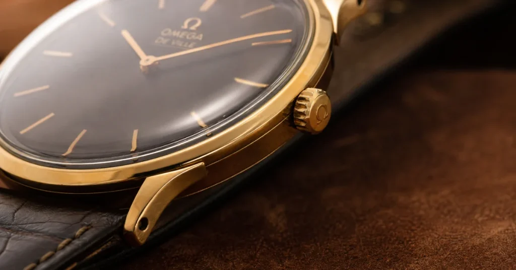De Ville Omega watch price: a macro of a gold De Ville case and crown with a dark dial on brown leather