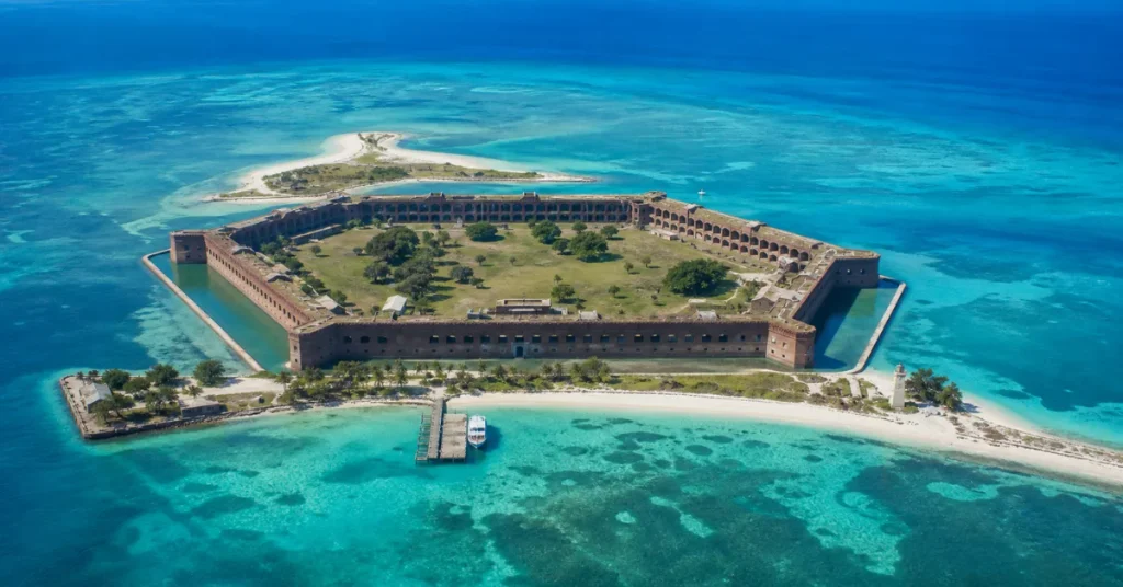 Most beautiful national parks in the US: an aerial of Fort Jefferson at Dry Tortugas National Park surrounded by turquoise water, a beach, and a boat dock
